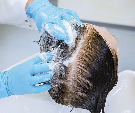 Eine Friseurin scheitelt das Haar der Probandin in der Mitte. Eine Seite w&auml;scht sie mit dem Stan&shy;dard-Shampoo, die andere mit einem Test&shy;produkt. (Foto: Stiftung Warentest)