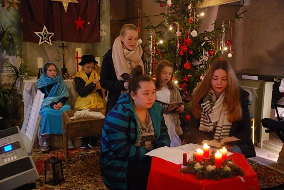 Bild: In dieser Szene sehen wir hinten Maria und Josef (Lotta und Leonhard) vor der Krippe sitzen, Letizia und Talia beim Singen des Liedes "Stille Nacht, heilige Nacht" und im Vordergrund Laura und Anna, welche die Rahmenhandlung spielen (Laura muss einen Aufsatz &uuml;ber Weihnachten schreiben, Anna erz&auml;hlt ihr die Weihnachtsgeschichte).