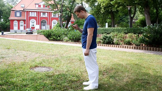 Bild: Andr&eacute; Johne, Praktikant in der Physiotherapie der HELIOS Klinik Bleicherode, simuliert die ungesunde Handyhaltung beim Blick auf sein Smartphone.