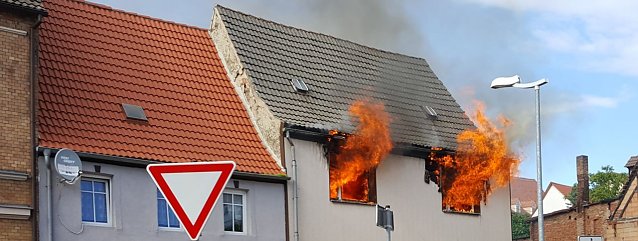 Bild: Flammen schlagen aus zwei Fenstern eines seit Jahren leerstehenden Geb&auml;udes in Hettstedt. Wenig sp&auml;ter treffen die ersten Feuerwehren vor Ort ein und bek&auml;mpfen den Brand. Das &Uuml;bergreifen der Flammen auf das Nachbarhaus kann verhindert werden.