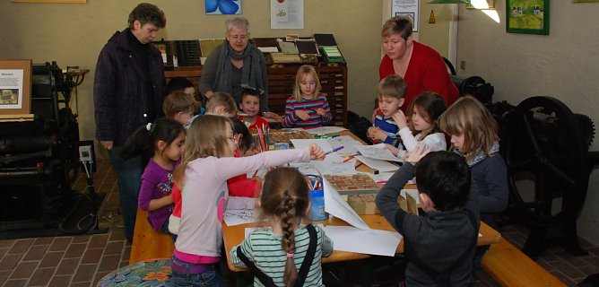 Renate Gr&uuml;neberg vom Druckereiverein und die Erzieherinnen Steffi Bastek und Carola Kr&ouml;ger (v. l.) betreuen die Kinder am Mal- und Stempeltisch im Vorraum der historischen Druckerei Heise. (Foto: Jochen Miche)