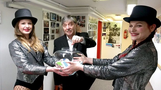 Er war f&uuml;r einen Konzertabend Hausmeister, Konzertmoderator und Gl&uuml;cksritter im Theater an der Landwehr in Eisleben: Schauspieler Reinhard Straube � bei der Verlosung wurde er von jungen Mitarbeiterinnen des Hauses charmant begleitet. (Foto: Kulturwerk Mansfeld-S&uuml;dharz)